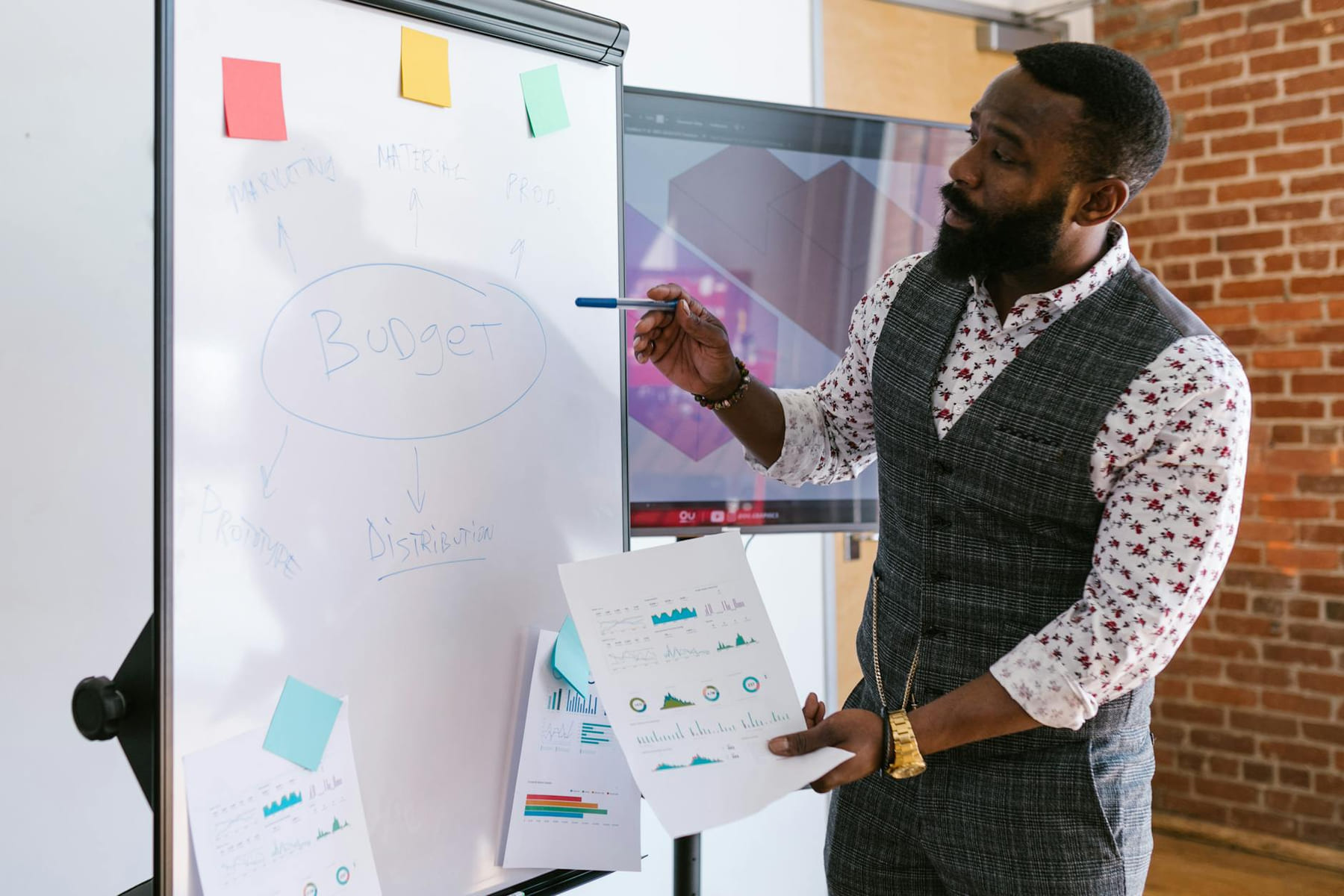 A businessman explains budget strategies using a whiteboard in an office setting. on Small Biz Blueprint