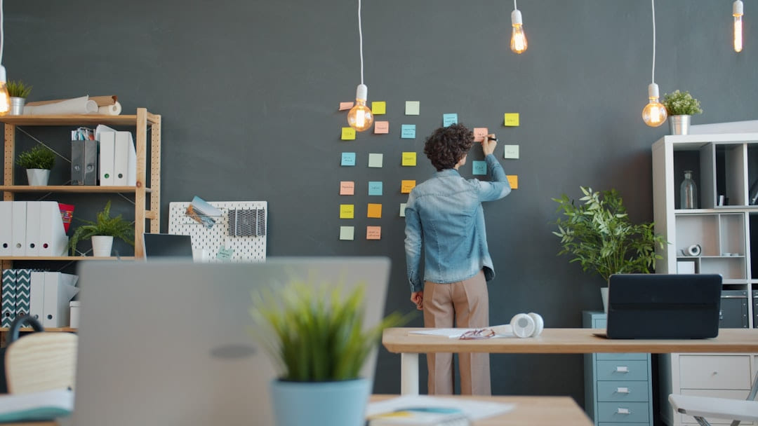 Person arranging sticky notes on a dark wall. on Small Biz Blueprint