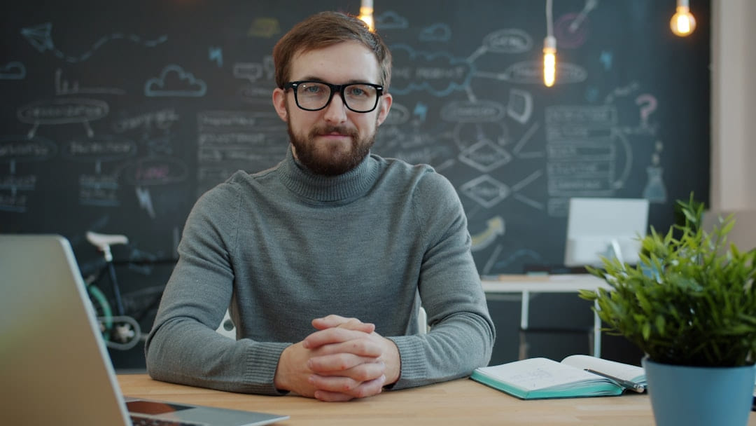 Man wearing glasses sits at a desk in office on Small Biz Blueprint