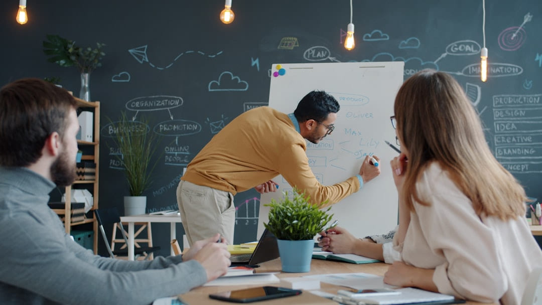 Man presenting ideas on whiteboard to colleagues on Small Biz Blueprint