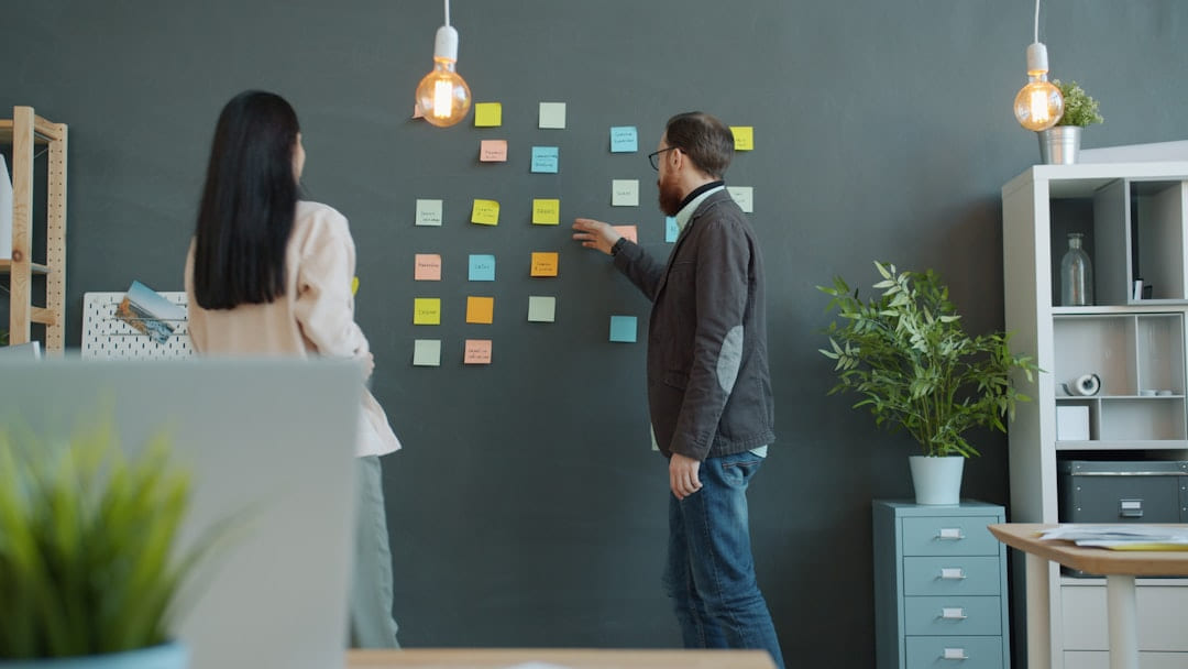 Two people planning with sticky notes on wall. on Small Biz Blueprint