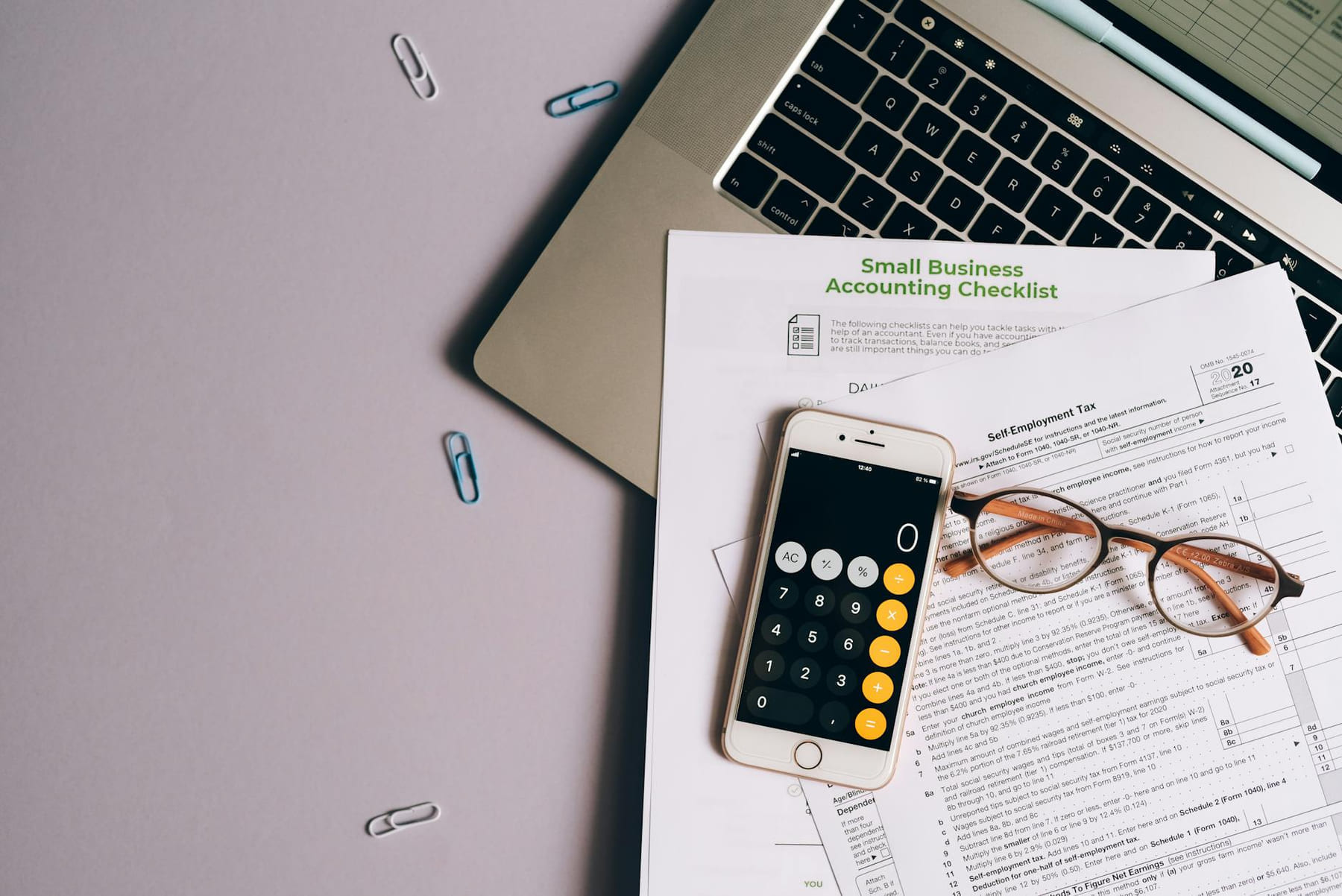 Flat lay of small business accounting tools including tax form, phone, and glasses on a desk. on Small Biz Blueprint