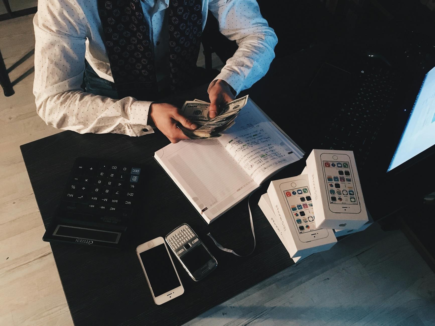 Businessman organizing finances with tech devices and cash on desk. on Small Biz Blueprint